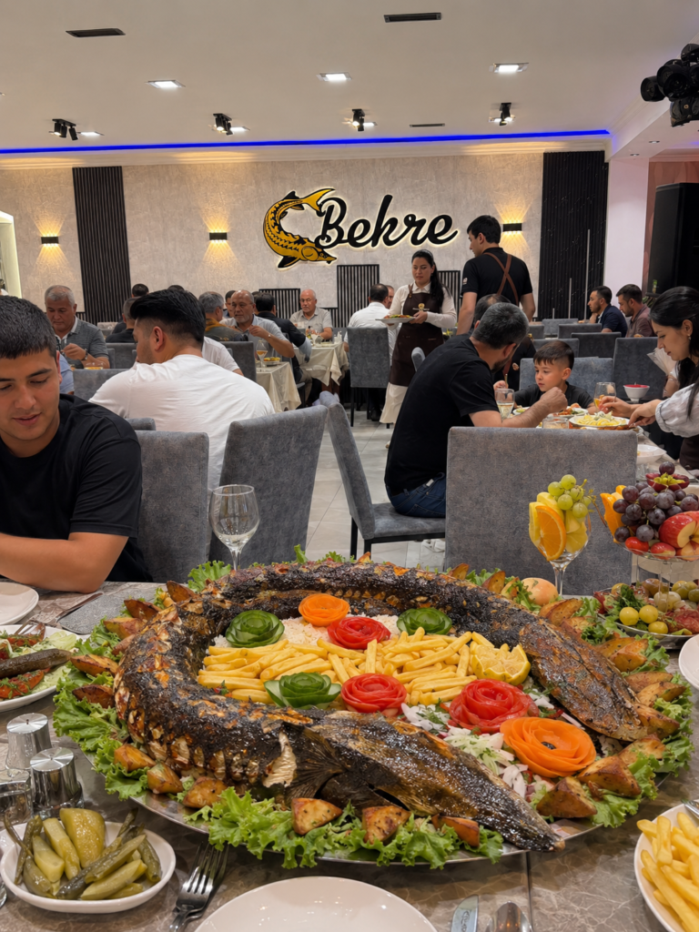 Whole grilled sturgeon platter served at a full table in Bekre restaurant, Türkmenbaşy